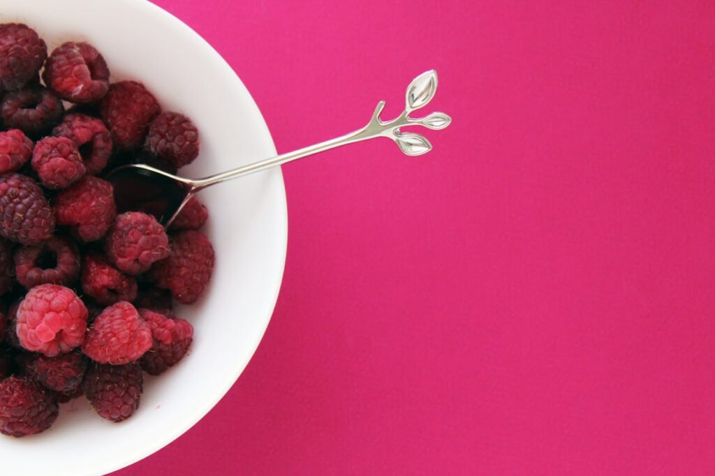 pexels-photo-1145977-1 A bowl of fresh raspberries with a spoon on a vibrant pink background, ideal for health-related themes.